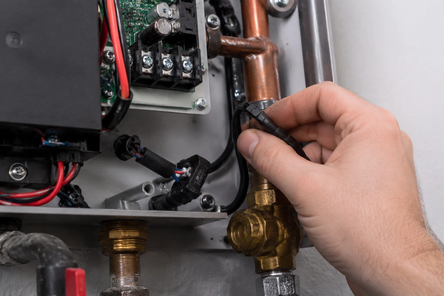 An EcoSmart electric tankless water heater opened with the breaker off, showing the inlet thermistor and its connector at the cold-water inlet being inspected