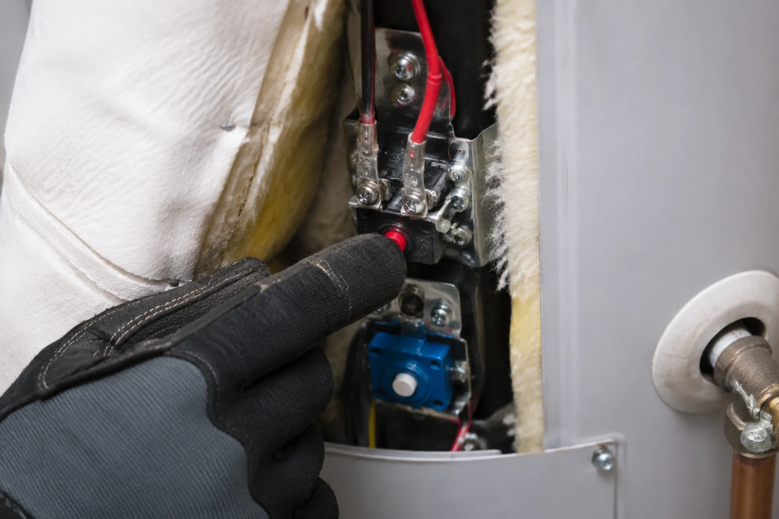 The upper thermostat of an electric water heater behind the open access panel, with the red ECO reset button, the temperature dial, and the element terminal screws visible