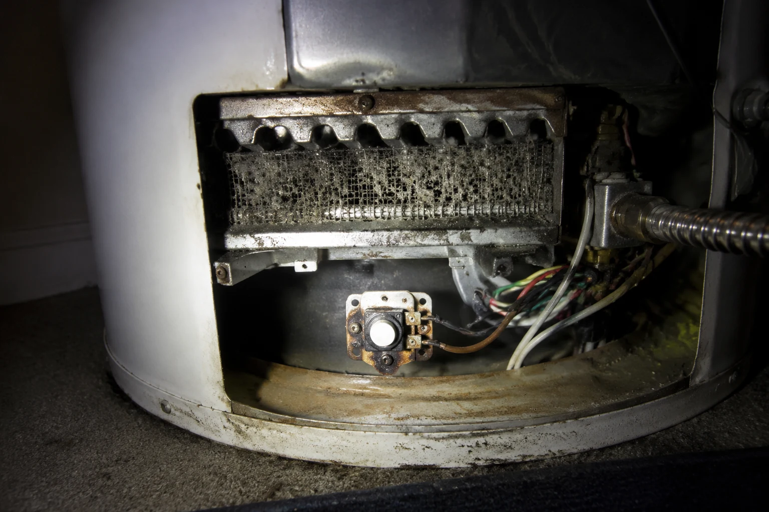 Technician vacuuming the lint-clogged flame-arrestor intake screen at the base of a gas water heater