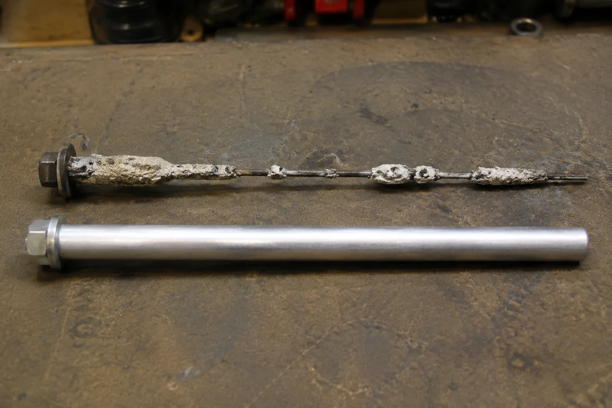 An old anode rod corroded down to its bare steel core wire next to a smooth new magnesium anode rod