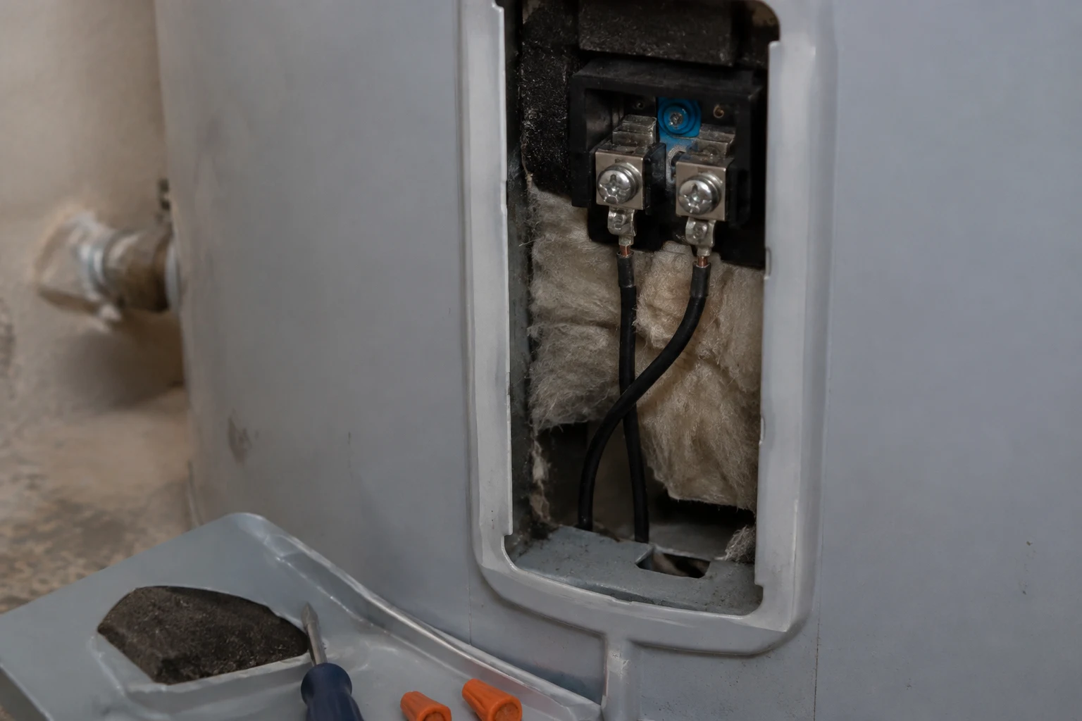Top junction box of an electric water heater with two hot leads under wire nuts and a bare ground on the green grounding screw, fed by a flexible whip