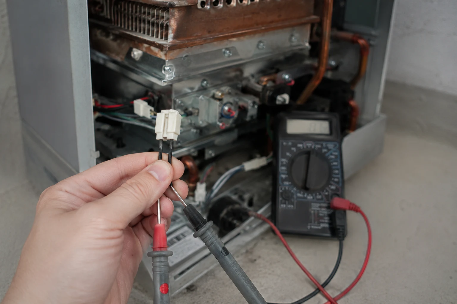 A Takagi heat-exchanger thermistor unplugged from its harness, being tested with a multimeter in the ohms range