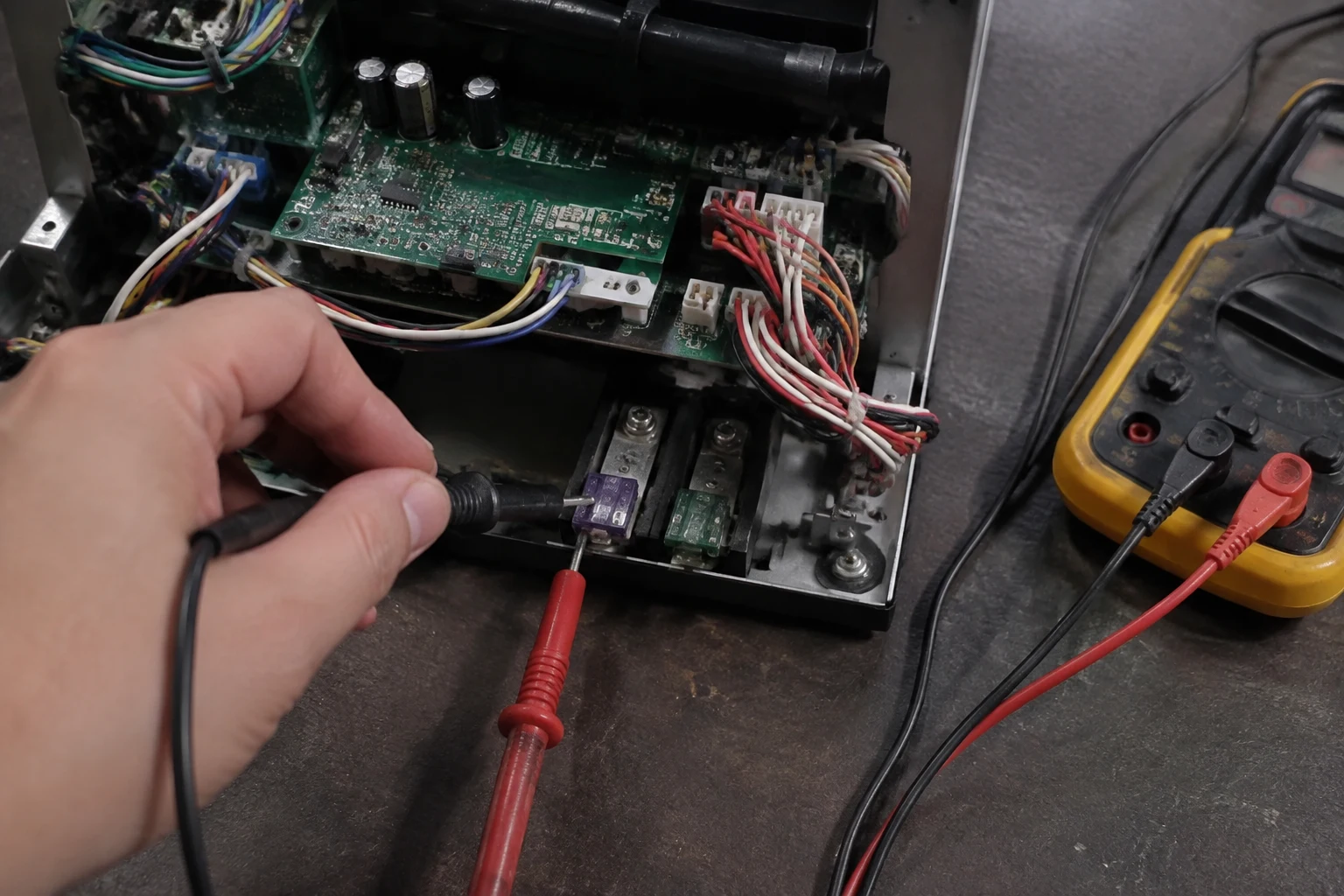 A Takagi tankless control board removed from the cabinet, with a technician inspecting the surge-box fuse and connectors for burn marks
