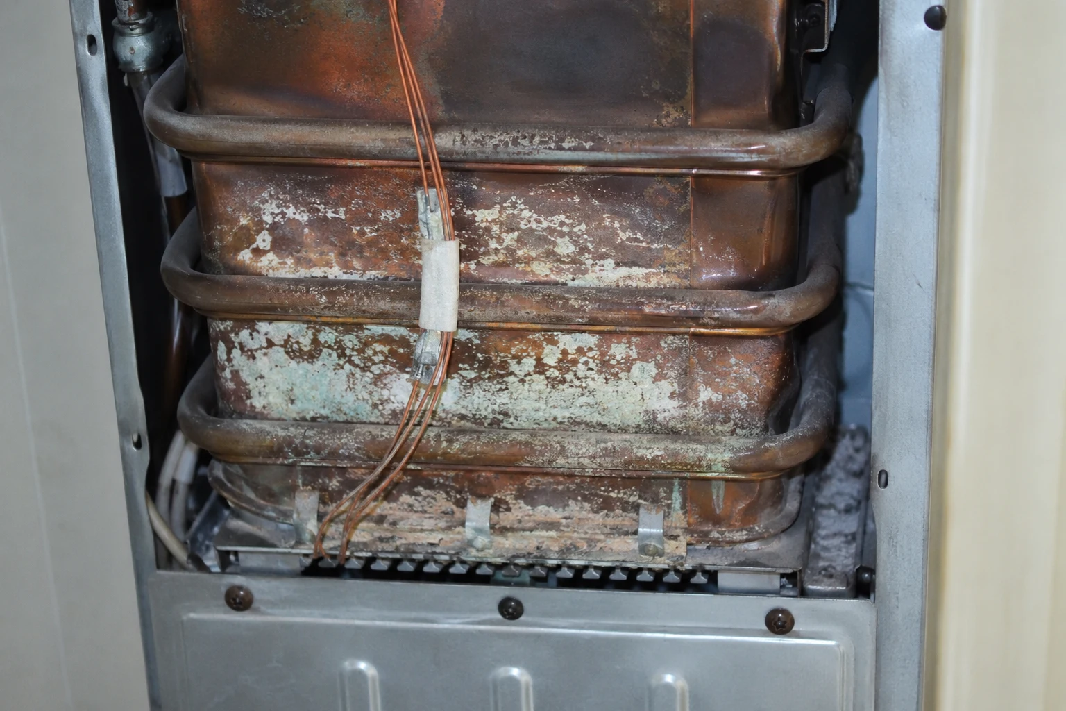 A tankless heat exchanger with the one-shot thermal fuse ribboned against the copper body, next to a control board showing an overheat error code