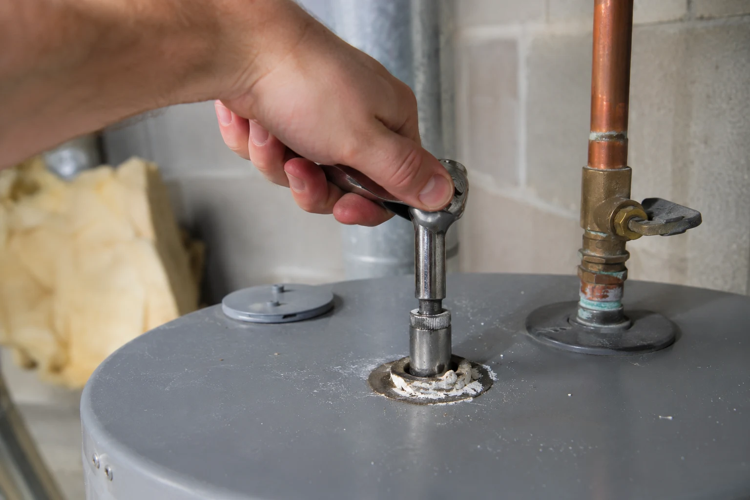A corroded magnesium anode rod pulled out of a water heater, heavily pitted and coated with dark buildup, held next to a new aluminum-zinc replacement rod for comparison