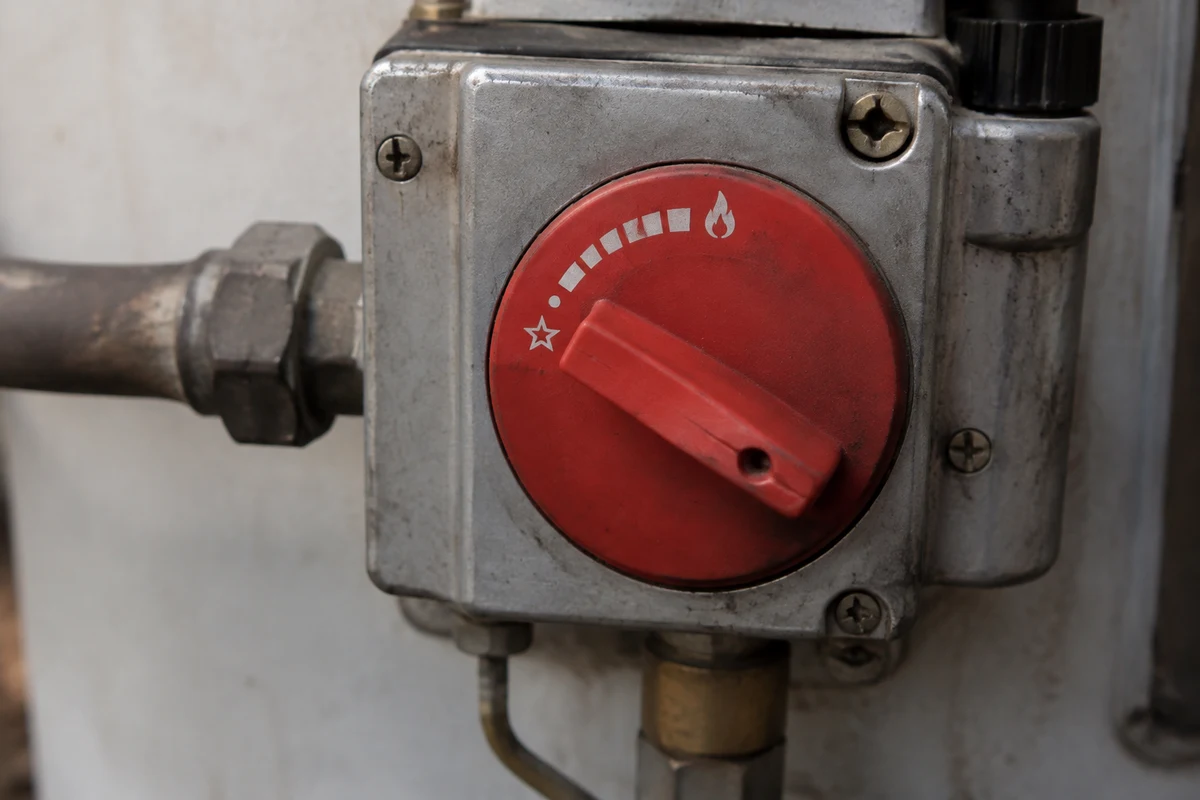 Red gas control dial on a water heater turned toward the low vacation setting